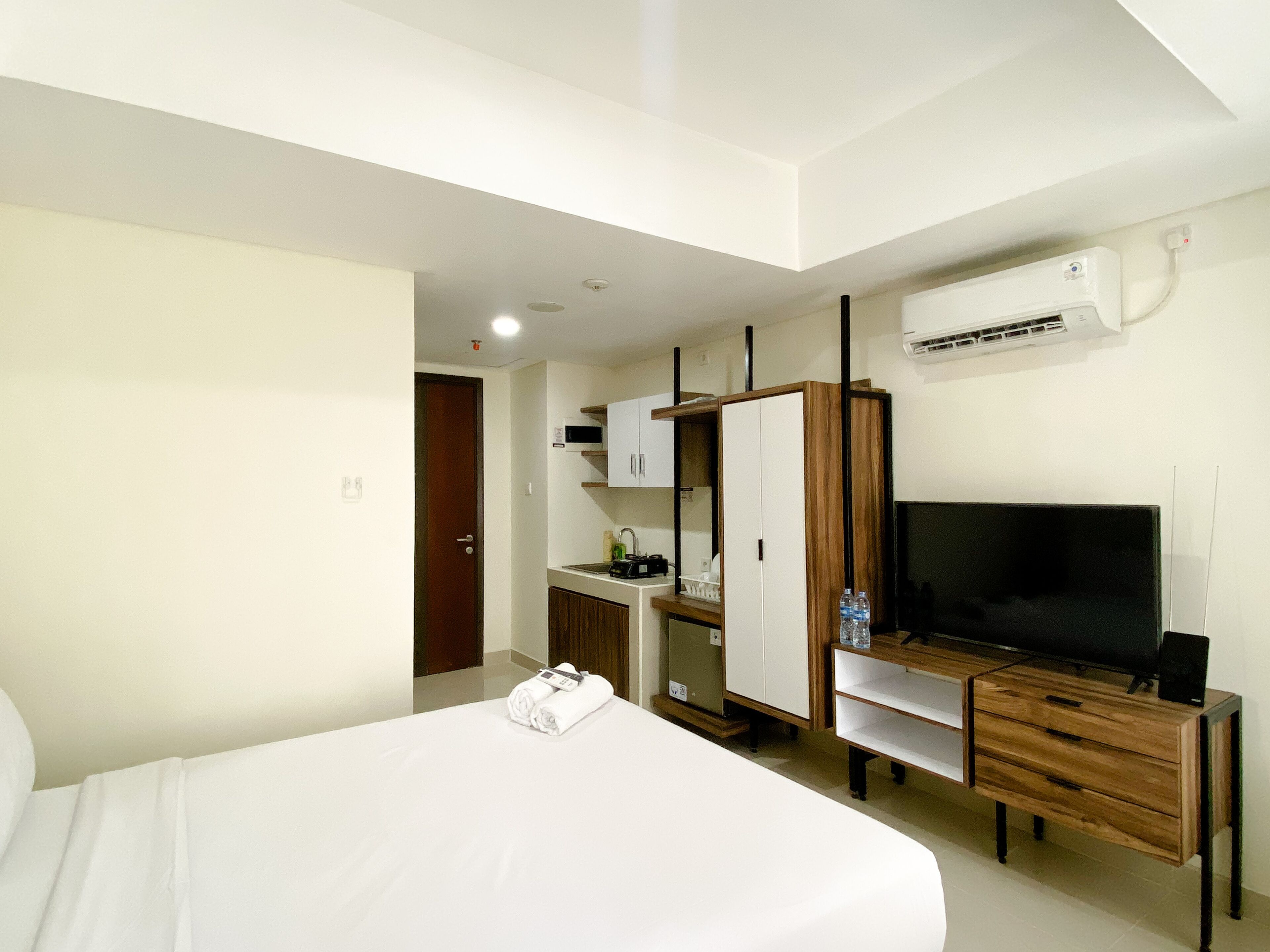 A hotel room with a bed, a desk with a TV, a wardrobe, and an air conditioning unit.