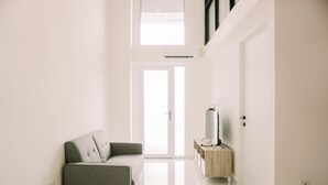 Sala de estar moderna com sofá cinza, mesa lateral de madeira e televisão, e uma grande janela que oferece iluminação natural.