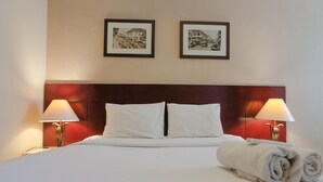 A neatly made bed with white linens, two framed pictures on the wall, and two bedside lamps. - Homey 2Br At Galeri Ciumbuleuit 1 Apartment (Bandung)