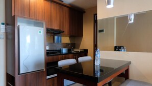 A compact kitchen with a refrigerator, stove, and a dining table with chairs. - Homey 2Br At Galeri Ciumbuleuit 1 Apartment (Bandung)