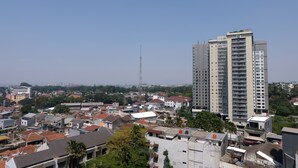 A high-rise building with multiple balconies, surrounded by a densely packed urban area with various buildings and some greenery. - Homey 2Br At Galeri Ciumbuleuit 1 Apartment (Bandung)
