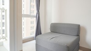 Un canapé gris est placé dans un coin d’une pièce dotée d’une grande fenêtre, de murs blancs et offrant une vue sur les bâtiments à l’extérieur.