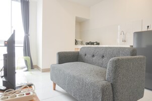 Una sala de estar con un sofá gris, un televisor y una mesita con un distribuidor de corriente.
