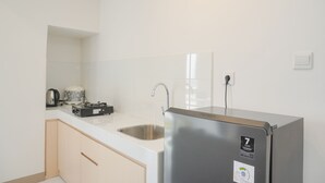 A compact kitchen with a stainless steel refrigerator, a sink, and a kettle.