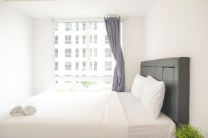 Una cama bien hecha con sábanas blancas, una cortina gris y vistas a un edificio a través de la ventana.