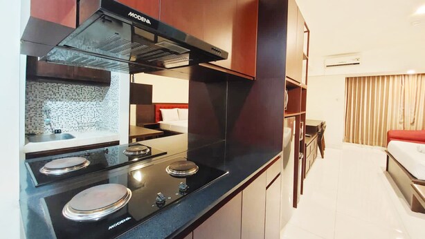 A modern kitchen with black appliances, a tiled backsplash, and wooden cabinets. - Brand New And Homey Studio At Mataram City Apartment (Ngaglik)