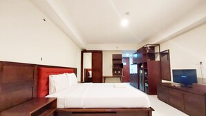 A hotel room with a large bed, wooden headboard, a desk with a chair, a television, and a wardrobe. - Brand New And Homey Studio At Mataram City Apartment (Ngaglik)