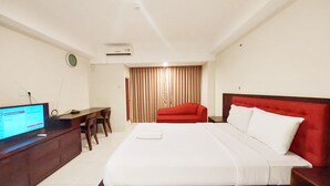A hotel room with a bed, a desk with a computer, a red chair, and a window with curtains. - Brand New And Homey Studio At Mataram City Apartment (Ngaglik)
