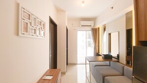 A modern living room with a sofa, a coffee table, and a TV. There is a door leading to another room and an air conditioning unit on the wall. - Nice And Homey 2Br At Citra Living Apartment (Jakarta)
