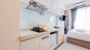 A modern hotel room with a kitchenette, a bed, a TV, and a window with curtains. - Comfy And Best Choice Studio At Sky House Bsd Apartment (Pagedangan)