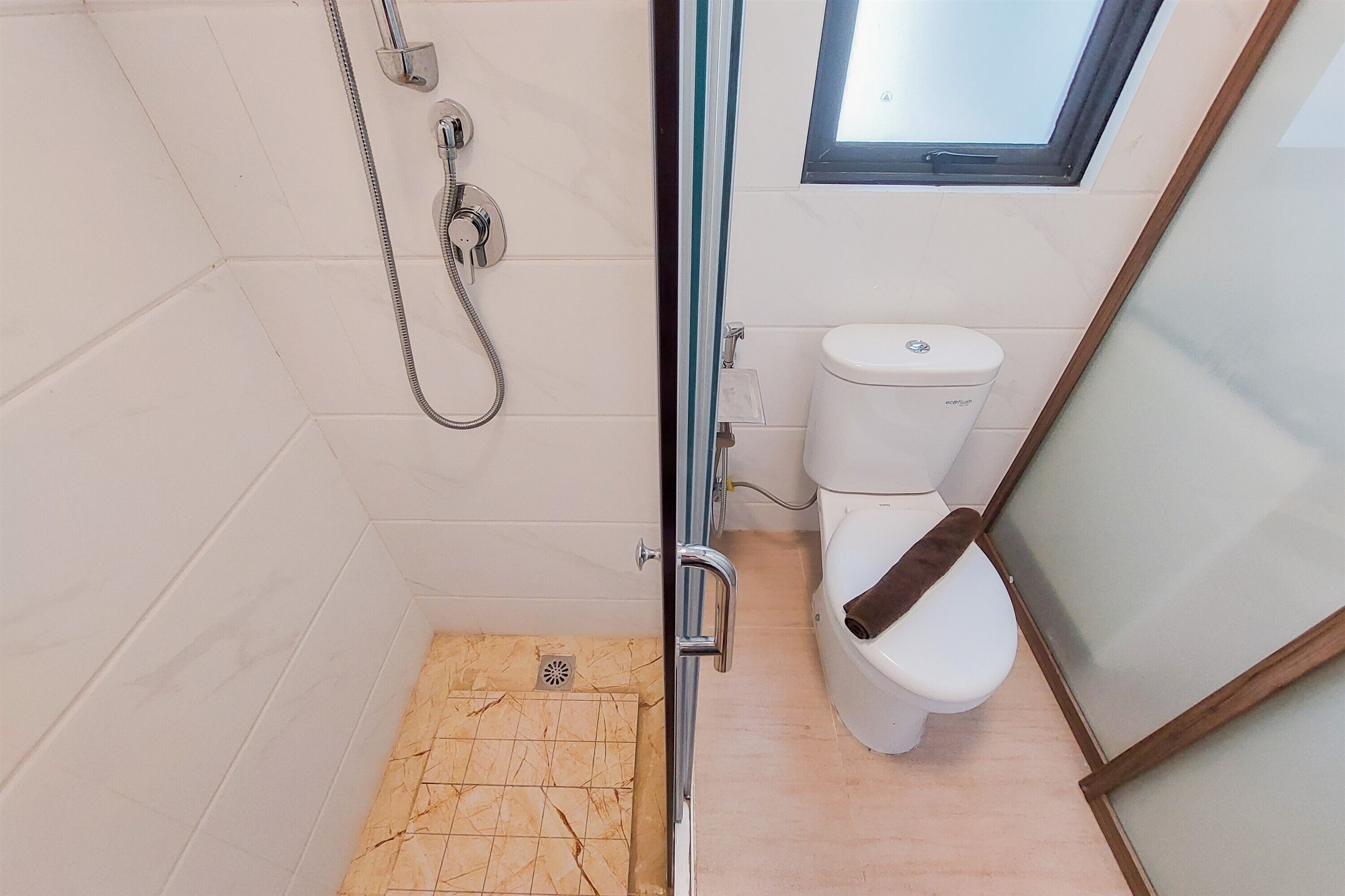 Een kleine badkamer met een douche, toilet en een raam boven het toilet.