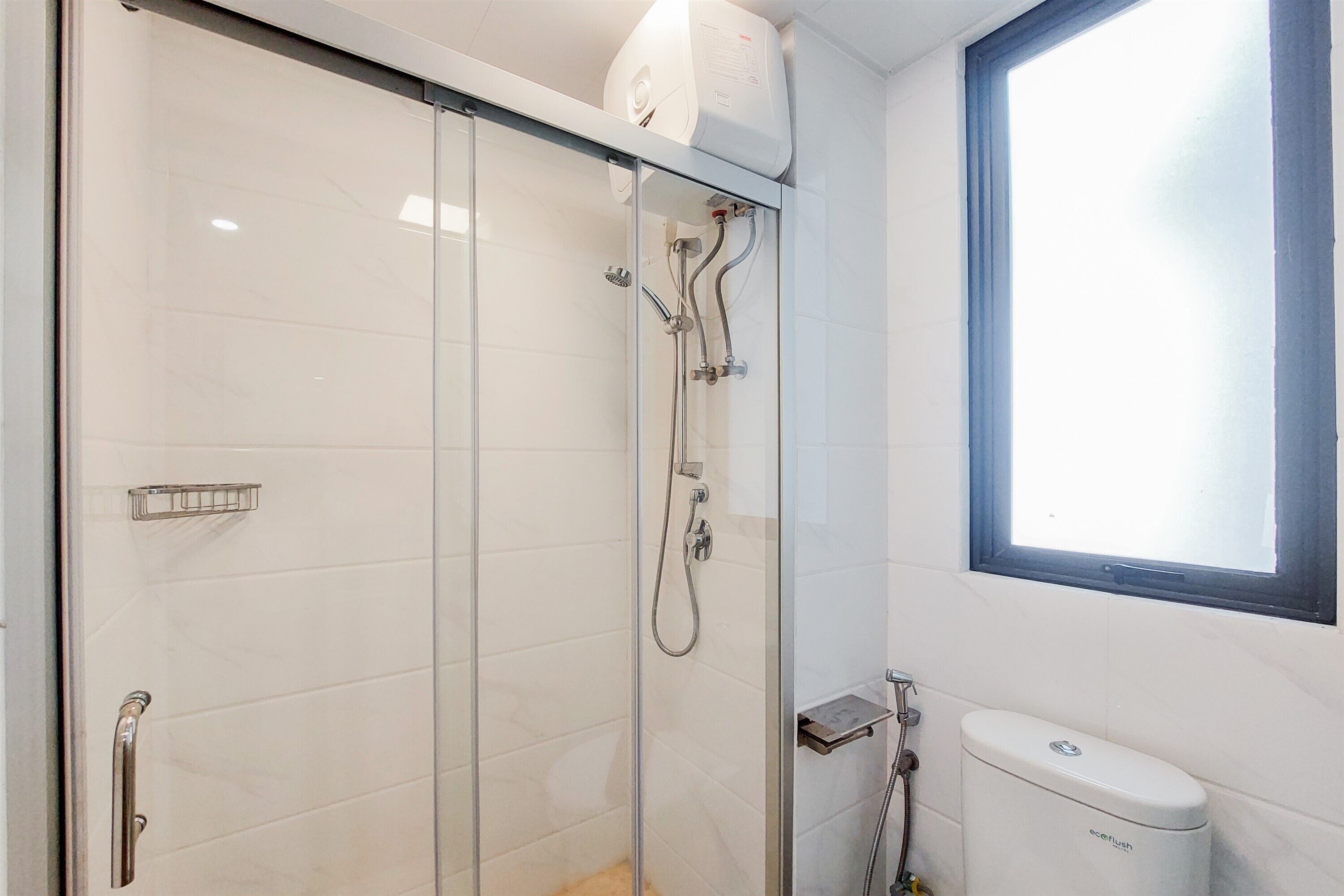 Et moderne badeværelse med en glasvægs brusekabine, toilet og et vindue med naturligt lys.