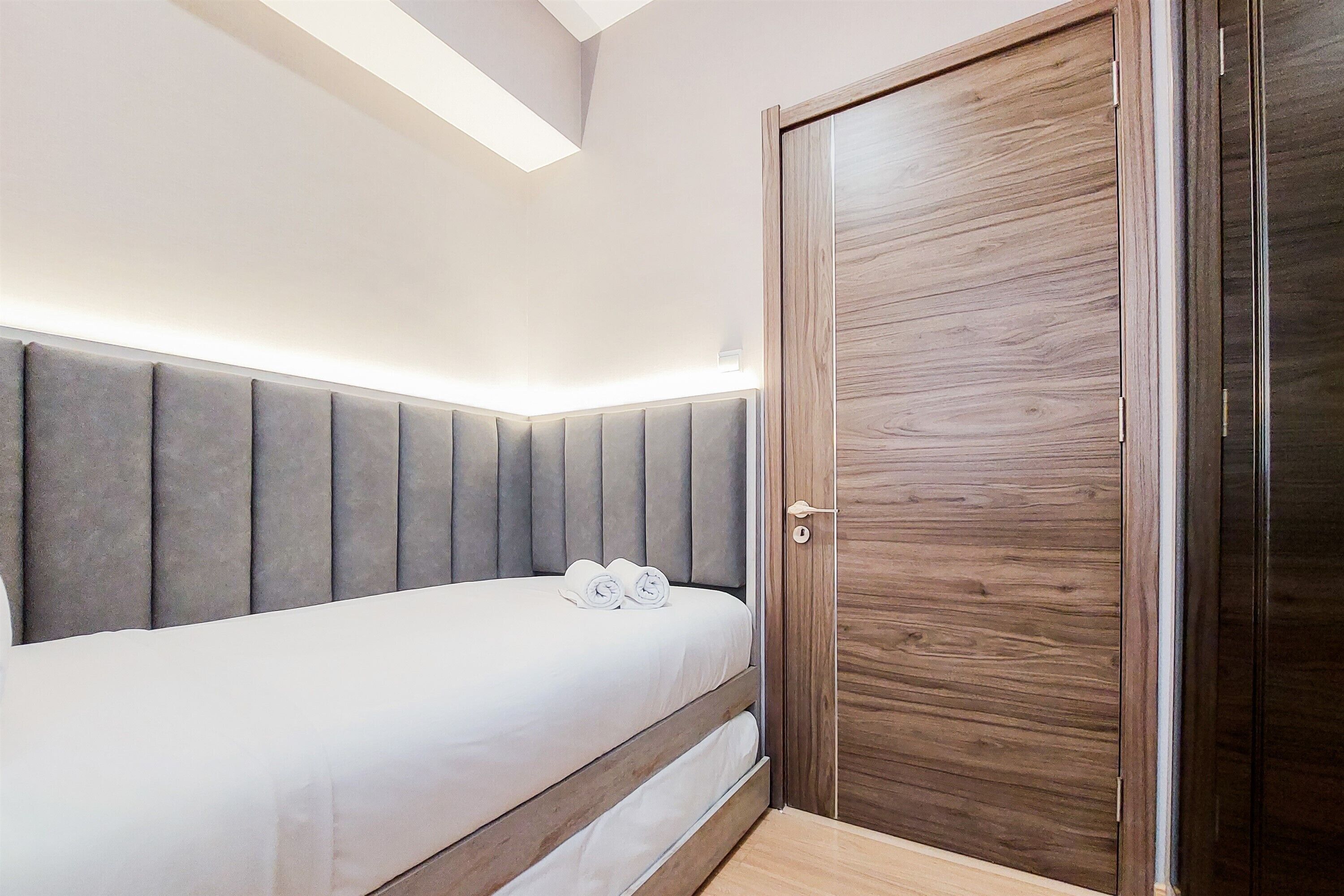 A bedroom with a bed, a wooden door, and a headboard with built-in lighting.