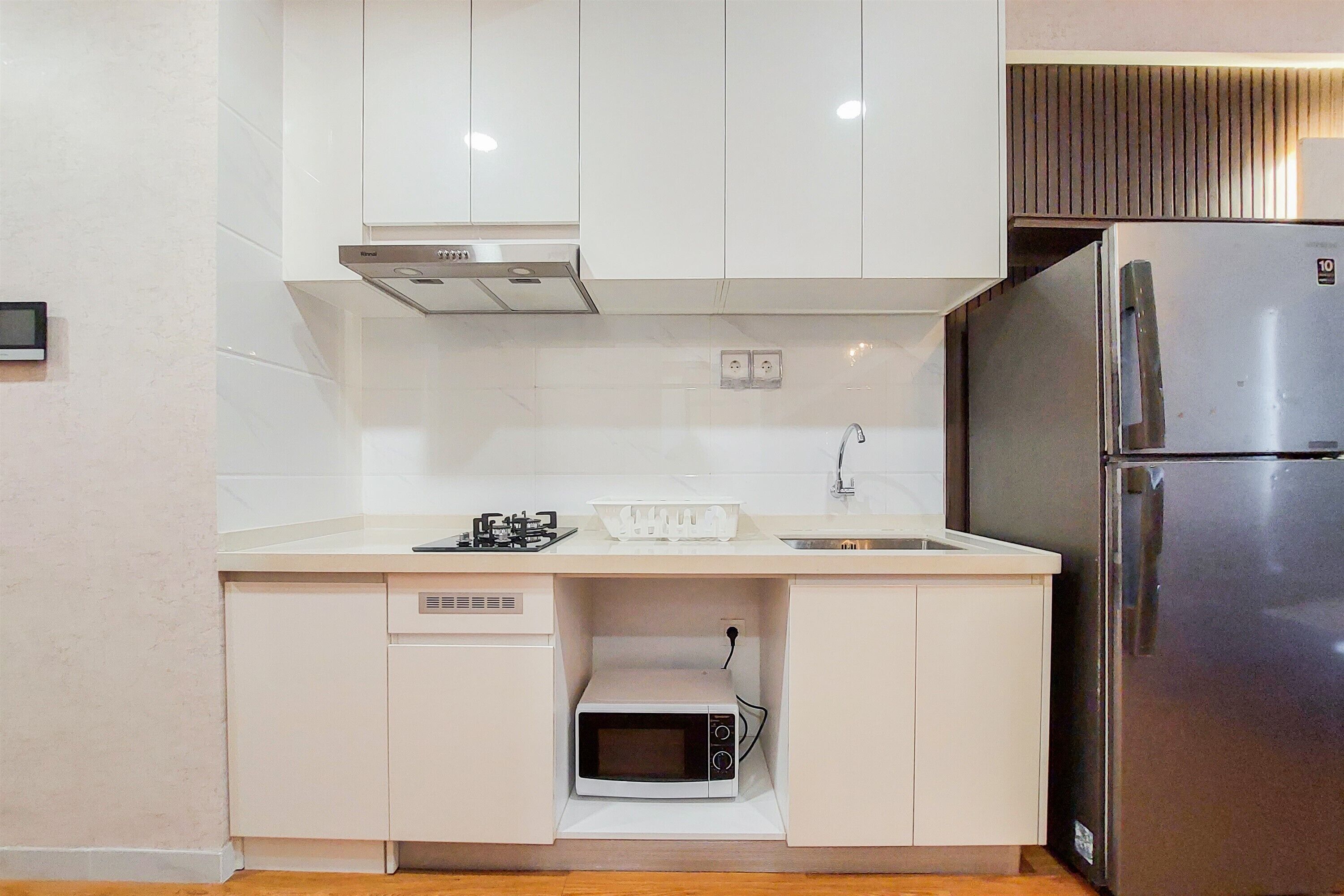 A compact kitchen with white cabinets, a built-in microwave, a stainless steel refrigerator, and a gas stove.