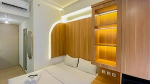 A hotel room with a bed, a wooden cabinet with illuminated shelves, a mirror, and a built-in air conditioning unit.