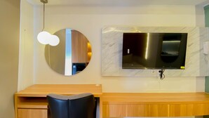 A modern room with a wooden desk, a black chair, a round mirror, and a flat-screen TV mounted on a marble wall.
