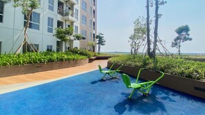 Une terrasse sur le toit avec un sol bleu, des appareils de musculation verts et une vue sur un bâtiment moderne doté de balcons et de verdure.