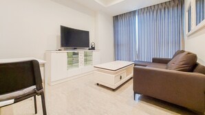 A modern living room with a flat-screen TV, a sofa, a chair, and a cabinet. - Homey And Tranquil 1Br Branz Bsd City Apartment (Pagedangan)