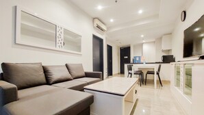A modern living room with a sofa, a coffee table, and a dining area with chairs and a table. - Homey And Tranquil 1Br Branz Bsd City Apartment (Pagedangan)