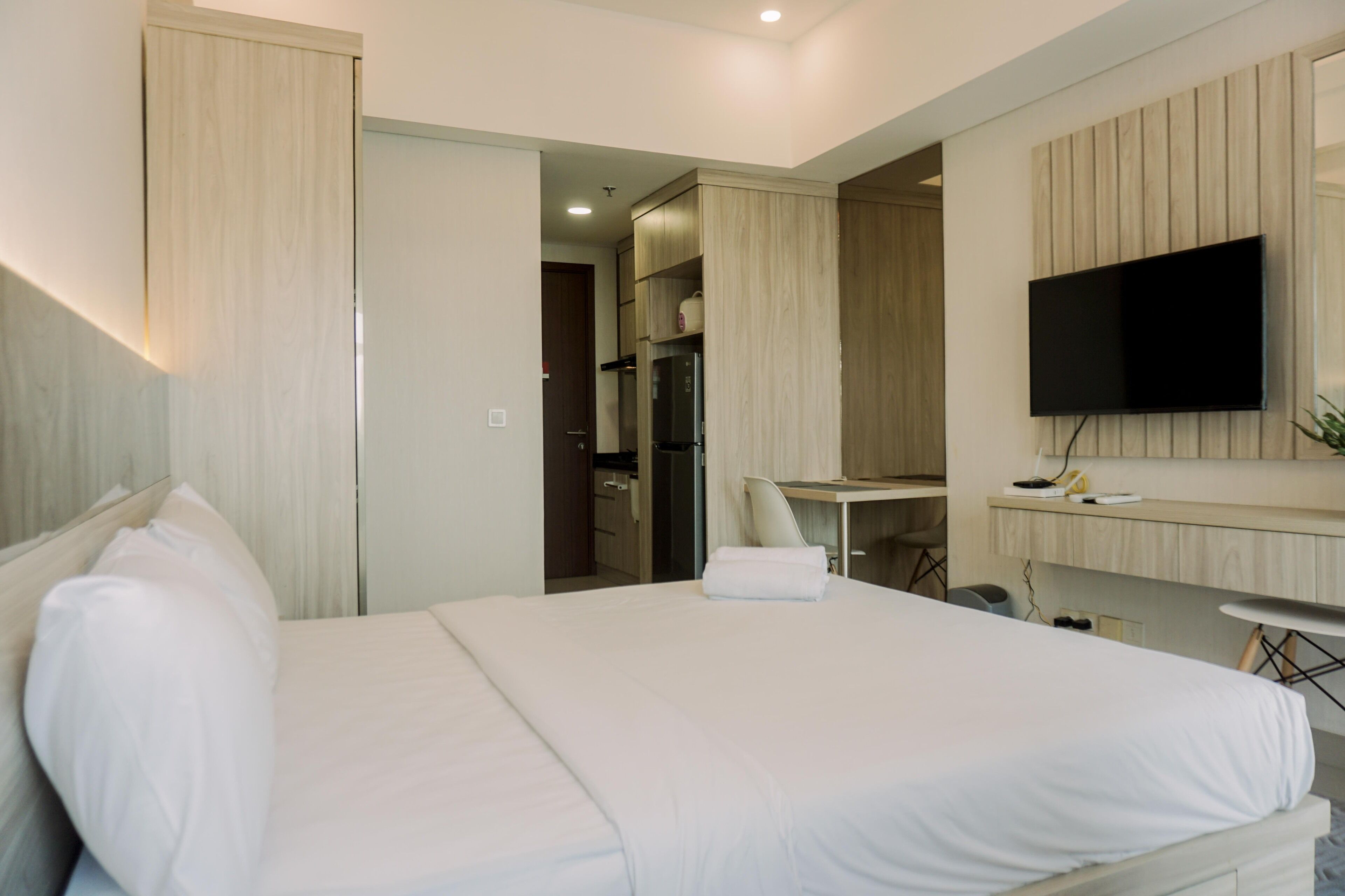A hotel room with a large bed, a desk, a flat-screen TV mounted on the wall, and a kitchenette area.