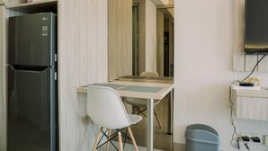 A compact kitchen with a refrigerator, a dining table with chairs, a TV mounted on the wall, and a trash bin.