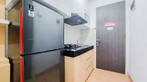 A compact kitchen with a black refrigerator, a stove, and wooden cabinets. - Warm And Cozy Living Studio Serpong Garden Apartment (Cisauk)