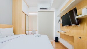A hotel room with a bed, a TV mounted on the wall, a bedside table, and a wardrobe. - Warm And Cozy Living Studio Serpong Garden Apartment (Cisauk)