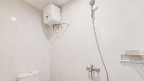 A bathroom with a toilet, a shower with a handheld showerhead, and a water heater mounted on the wall. - Warm And Cozy Living Studio Serpong Garden Apartment (Cisauk)