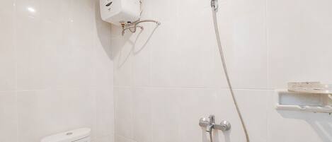 Un baño con inodoro, ducha con cabezal de ducha manual y calentador de agua instalado en la pared.