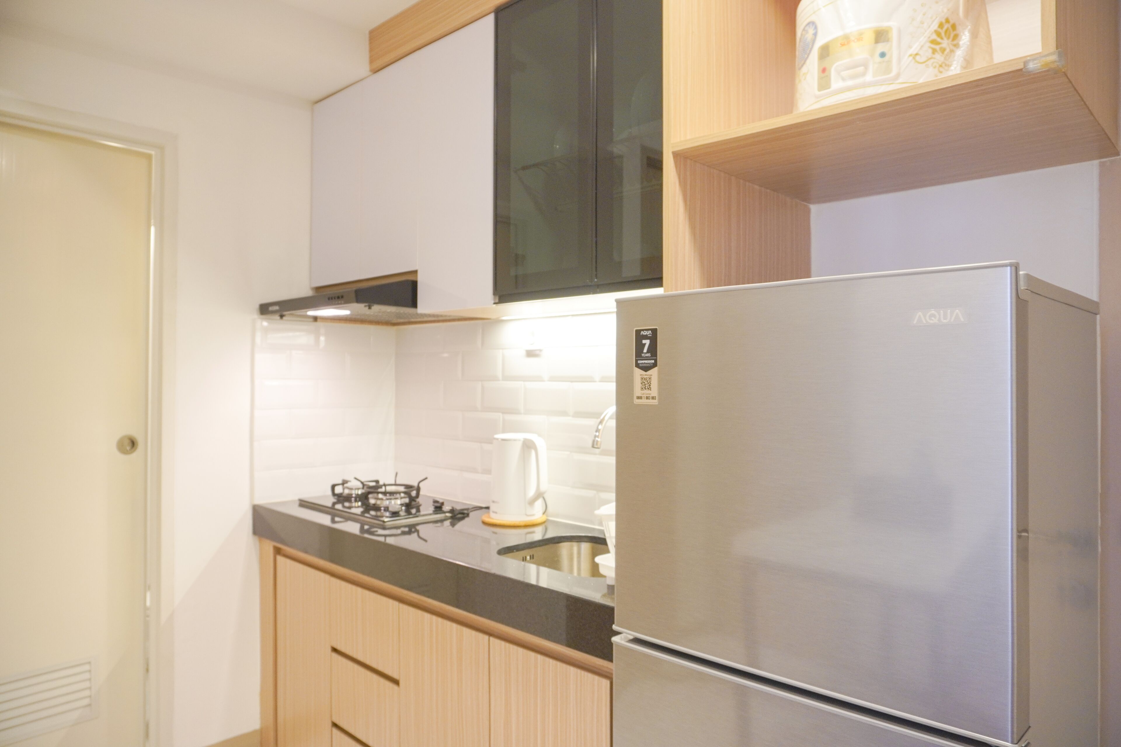 Cozinha moderna com geladeira de aço inoxidável, fogão a gás e paredes com azulejos brancos.