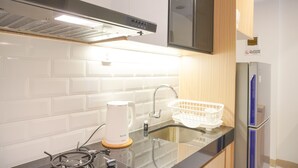 Une cuisine moderne avec un dosseret de carrelage blanc, une hotte noire, une bouilloire blanche, un évier avec un panier blanc et un réfrigérateur bleu.
