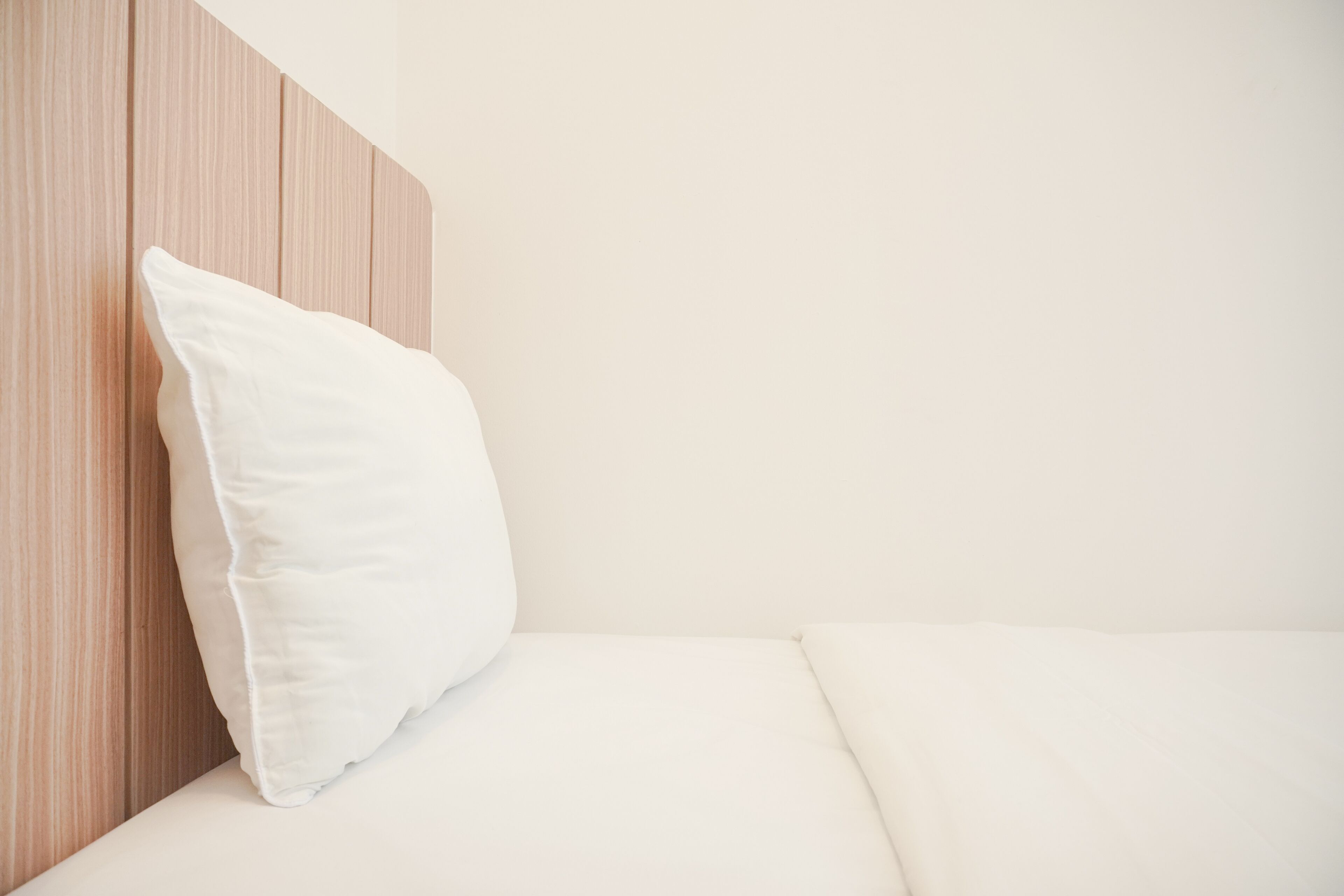 A neatly made bed with a white pillow and a wooden headboard.