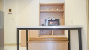 Un petit coin cuisine avec un meuble en bois, un plan de travail noir et une étagère où sont disposées des bouteilles d’eau et un panneau indiquant « Travelio ».