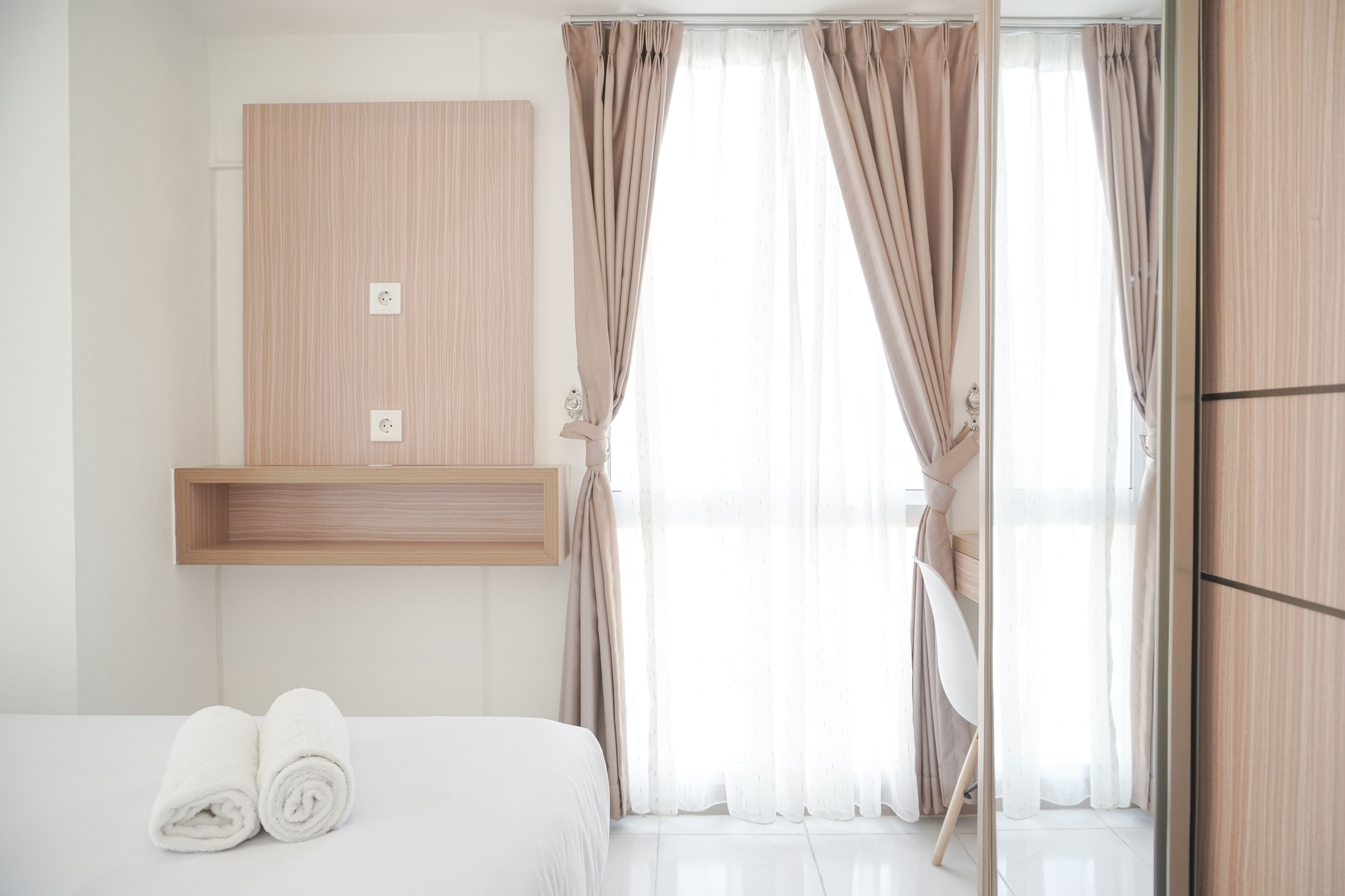 Una camera d'albergo con un letto, una mensola in legno e una finestra con tende.