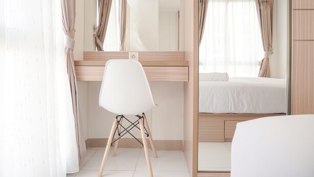 Une chambre d’hôtel moderne avec un bureau en bois, une chaise blanche, un lit et un grand miroir.