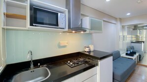 A modern kitchen with a built-in microwave, stainless steel sink, and a gas stove. - Homey And Modern 1Br At Kebagusan City Apartment (Jakarta)