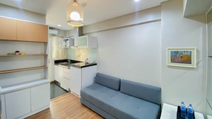 A modern kitchen with white cabinets, a grey sofa, and a dining table with water bottles. - Homey And Modern 1Br At Kebagusan City Apartment (Jakarta)