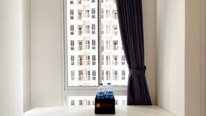 Ein Fenster mit Blick auf ein Gebäude, ein weißes Regal und zwei Wasserflaschen.