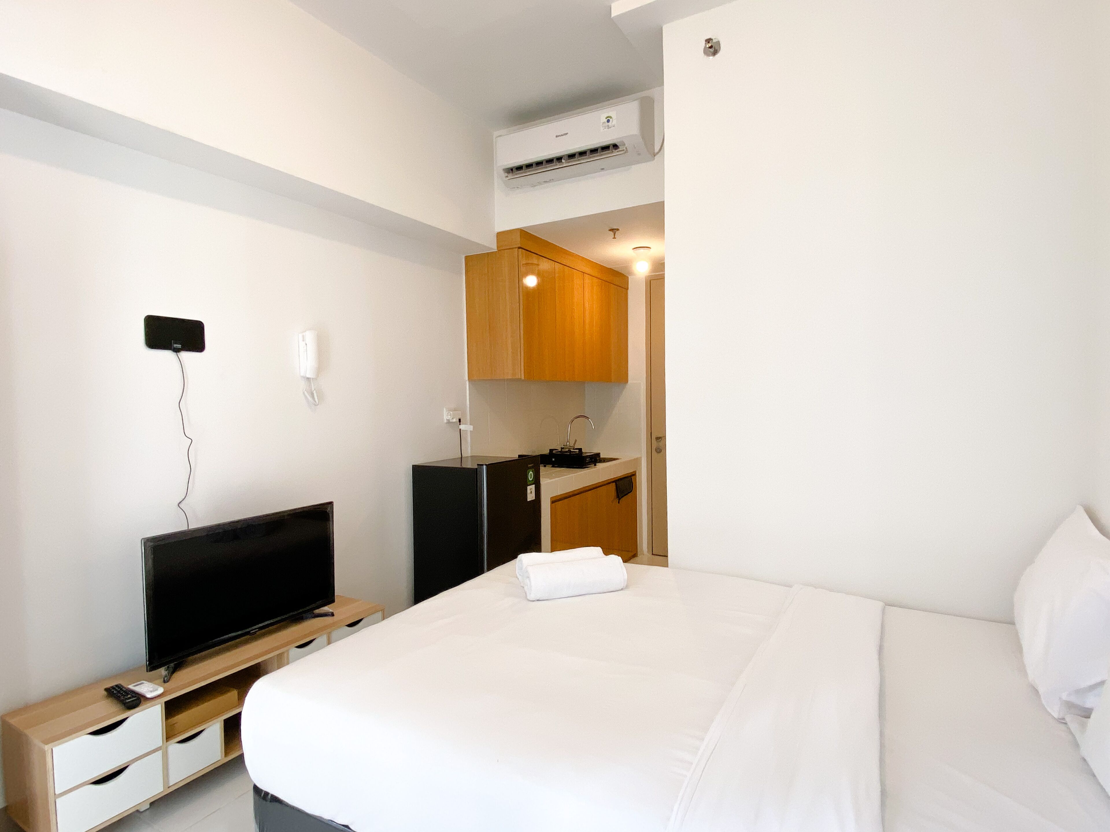 Ett hotellrum med en säng, en tv på ett träställ, ett litet pentry och en luftkonditioneringsanläggning.