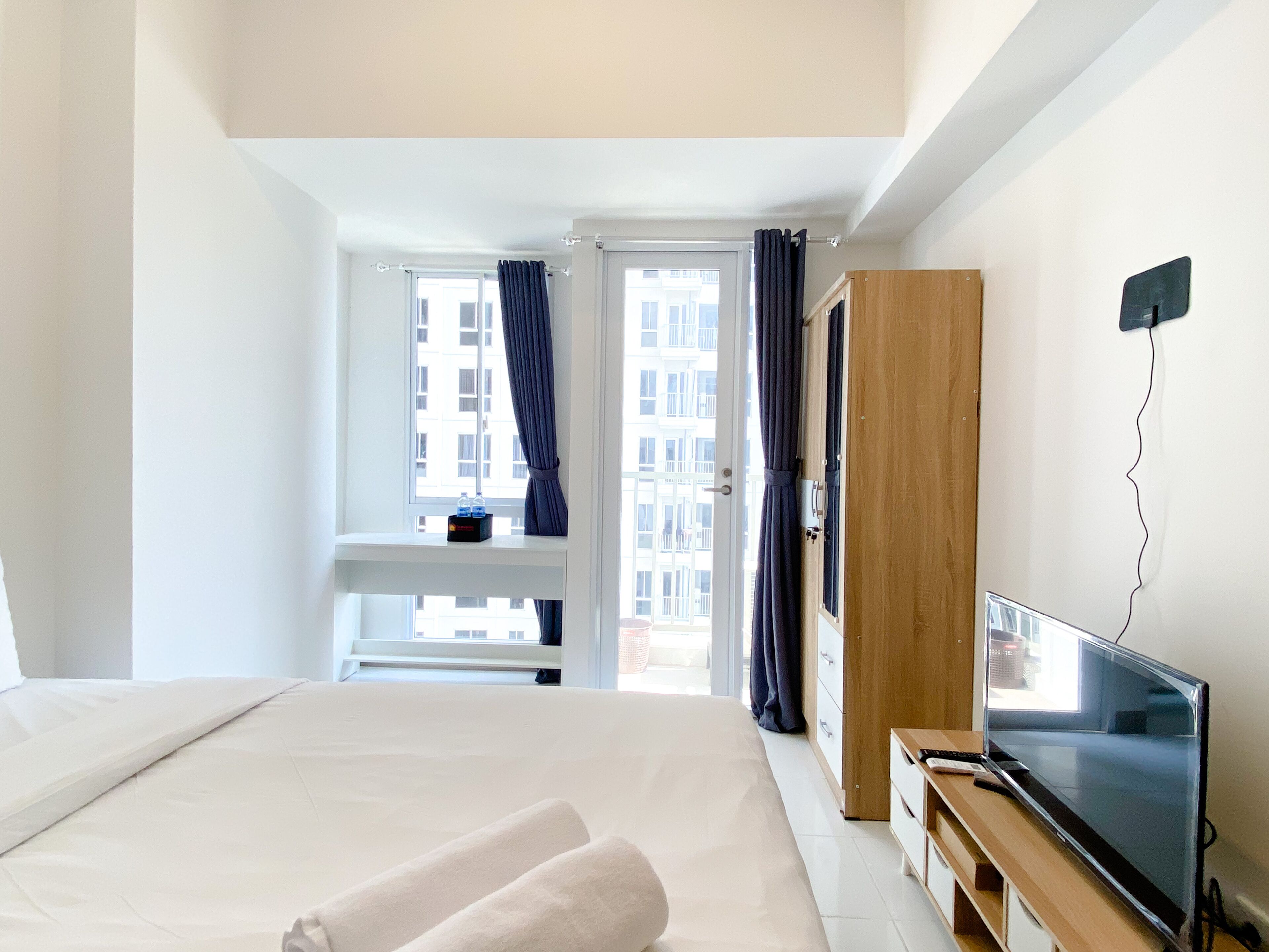 Une chambre d’hôtel avec un lit, une télévision, une armoire en bois et une fenêtre avec des rideaux.