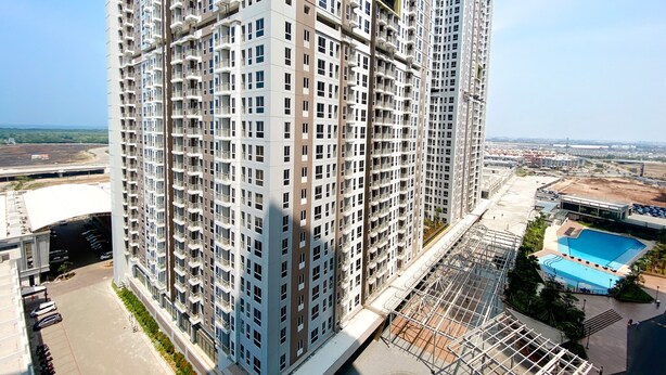 En høj bygning med lejligheder, flere balkoner, en swimmingpool og udsigt over det omkringliggende område.