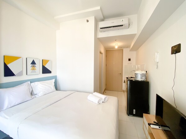 A hotel room with a bed, a TV, an air conditioner, and a small desk with a remote control.