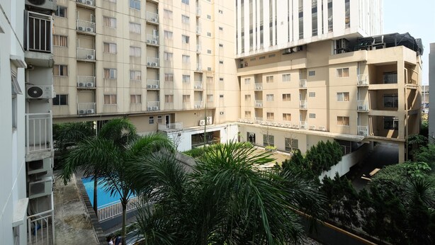 A multi-story residential building with balconies, a swimming pool, and surrounding greenery. - Nice 2Br At Bogor Valley Apartment (Bogor)