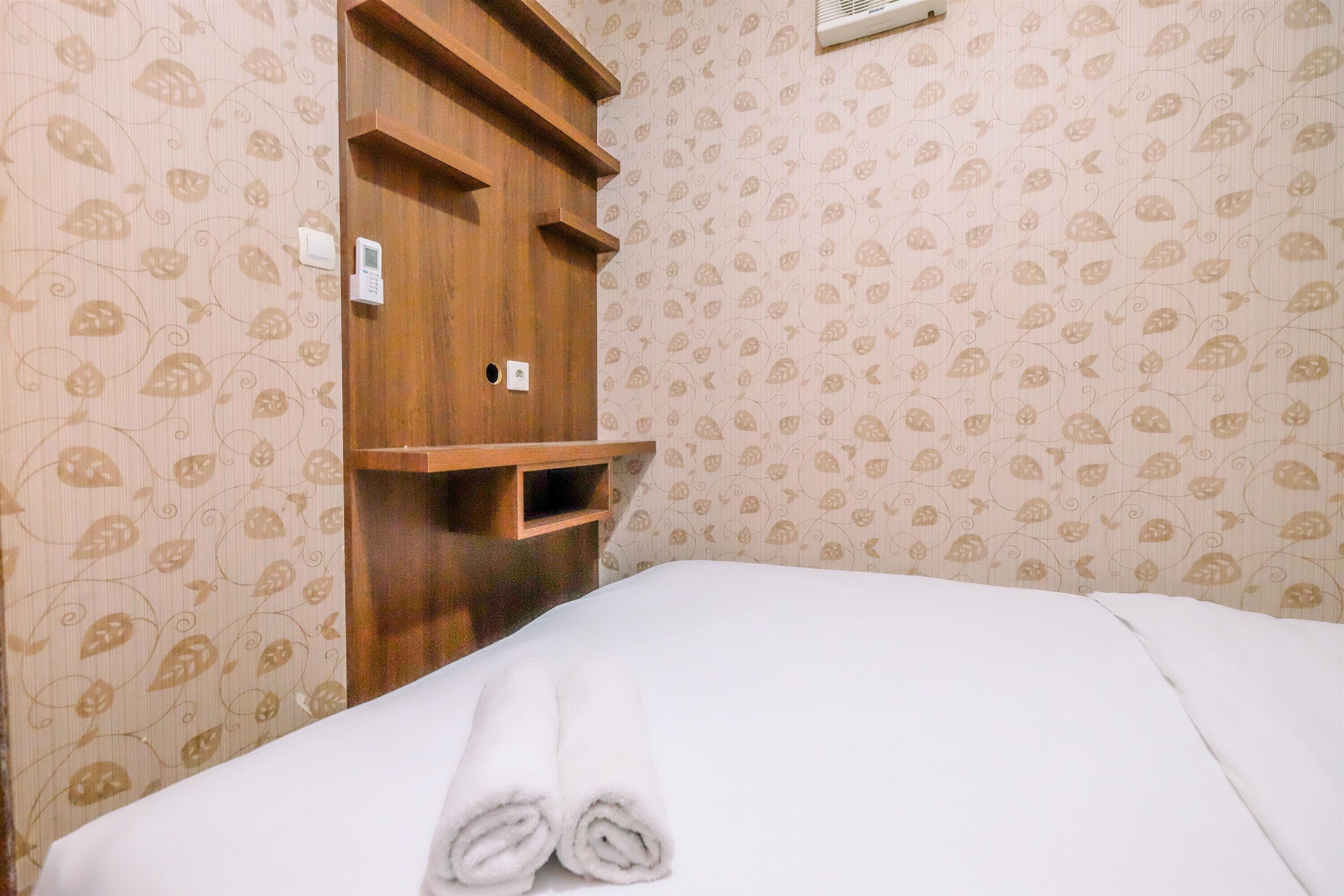 A hotel room with a bed, a wooden shelf unit, and patterned wallpaper.