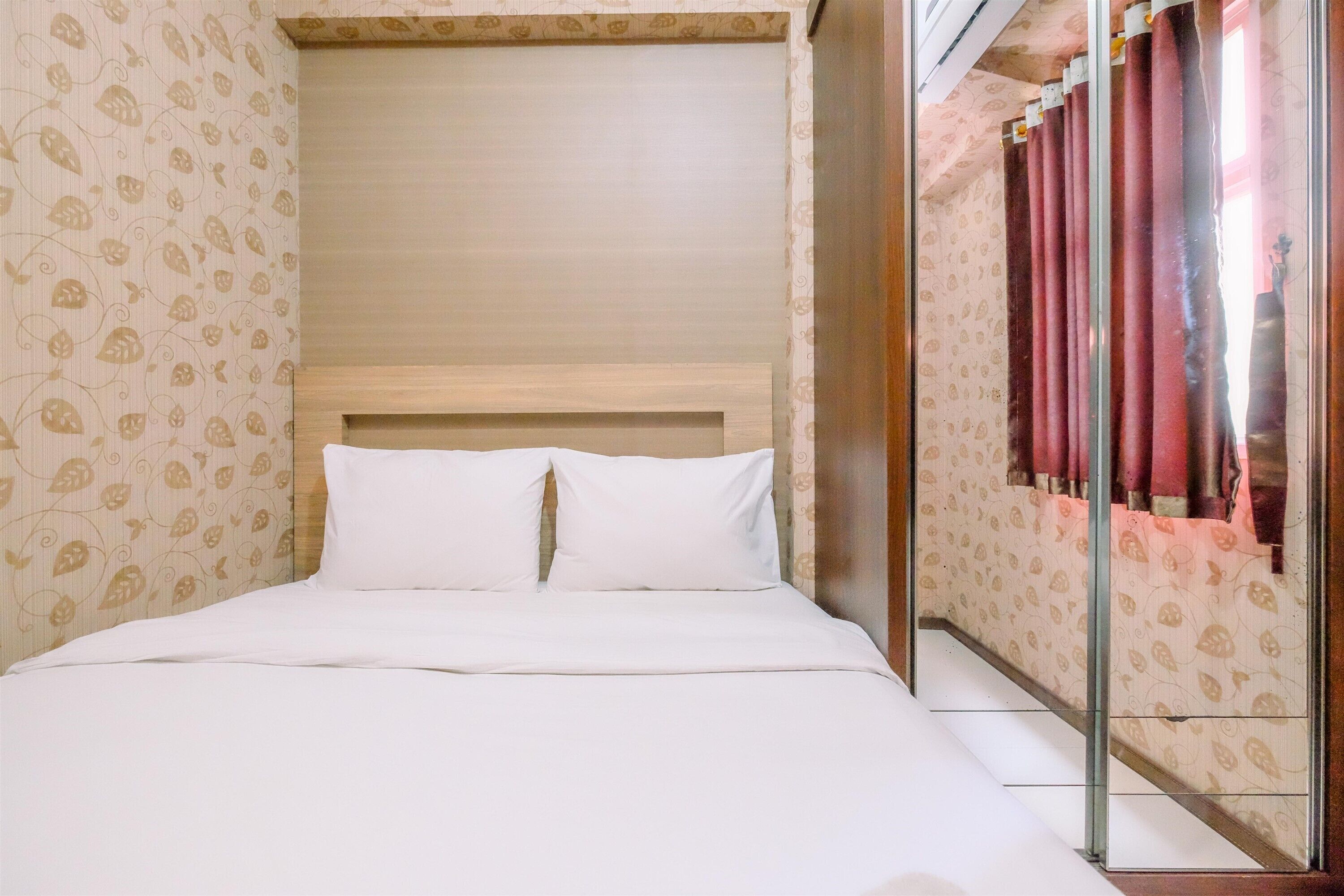 A hotel room with a bed, a wooden headboard, patterned wallpaper, and a sliding door with curtains.