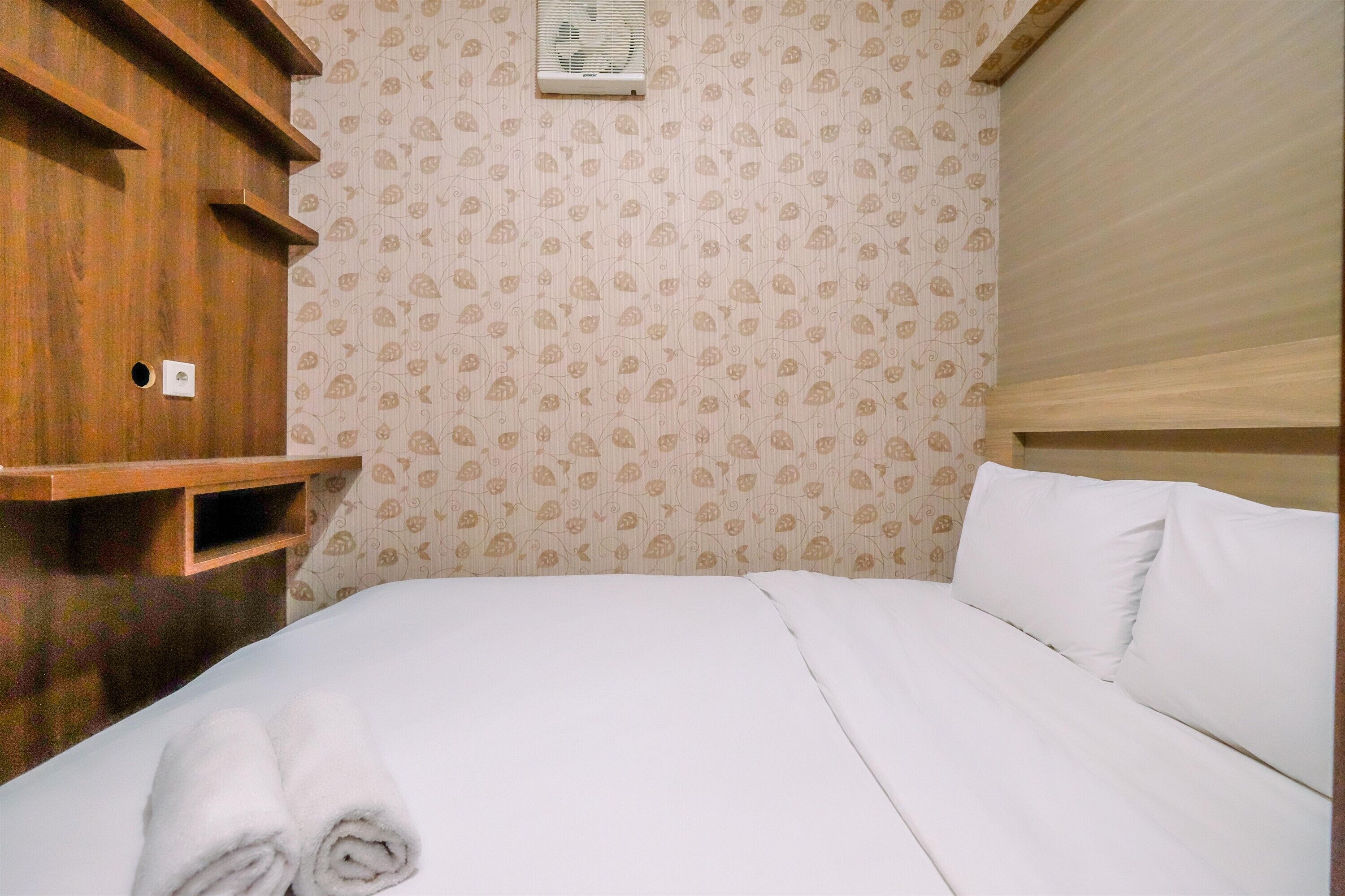 Una cama bien hecha con ropa blanca, un aparador de madera con repisas abiertas y un papel tapiz estampado.