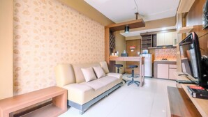A modern living room with a sofa, a coffee table, and a TV. There is a kitchen area with cabinets and a microwave. - Nice 2Br At Bogor Valley Apartment (Bogor)