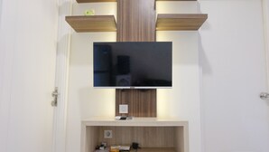 A wall-mounted TV with a wooden shelf below it, containing a few items. - Strategic And Comfortable 1Br Apartment At Parahyangan Residence (Bandung)