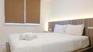 A neatly made bed with white linens and rolled towels, a wooden headboard, and a window with brown blinds. - Strategic And Comfortable 1Br Apartment At Parahyangan Residence (Bandung)