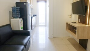 A modern kitchen with a refrigerator, water dispenser, and a flat-screen TV on a wooden shelf. - Strategic And Comfortable 1Br Apartment At Parahyangan Residence (Bandung)
